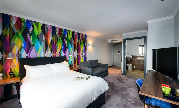 Double bed, sofa, desk and chair, TV and door leading to en-suite shower room.